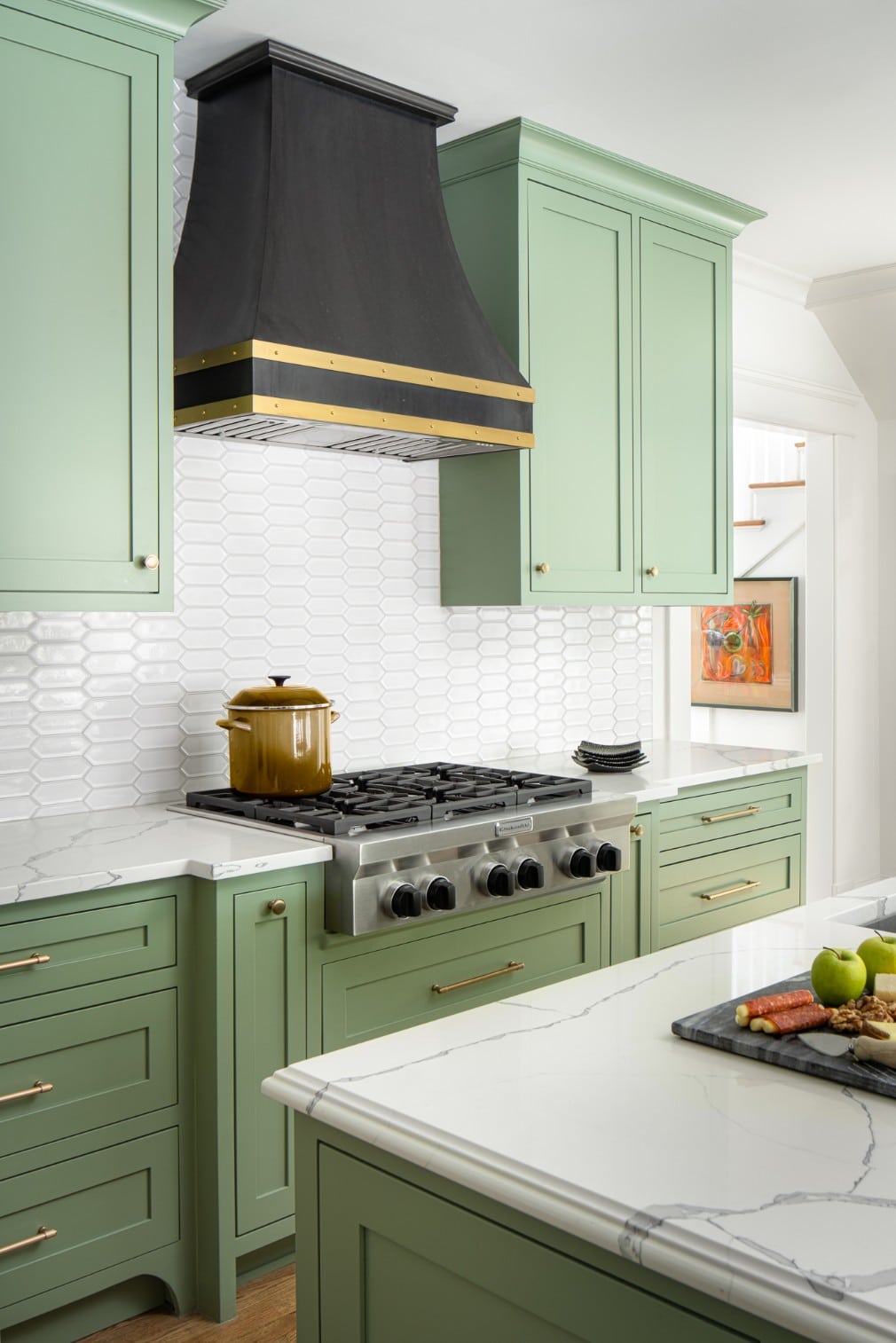 Transitional kitchen with green cabinetry, island, and black and brass range hood.