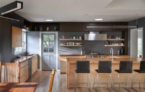 Mid century modern kitchen with dark walls, natural wood cabinetry, and open shelving.