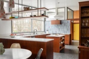 Mid Century Modern kitchen with natural wood flat-panel cabinets, white counters, open shelves, and custom blue backsplash tile.