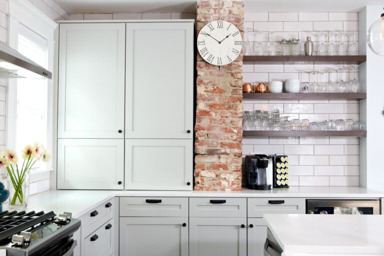 Gourmet kitchen with white cabinets, white counters, open shelving, white subway tile, and brick accent beam.