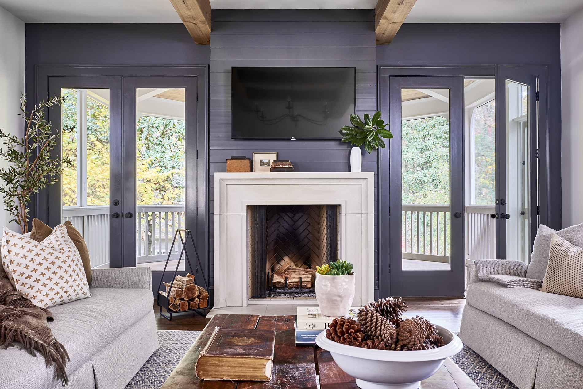 Moody transitional home living room with dark blue accent wall and double doors beside a stone wood burning fireplace.