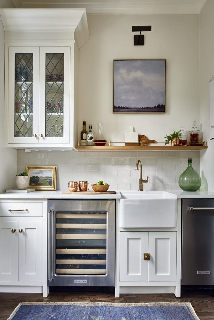 Transitional home bar with small farmhouse sink, leaded glass cabinet doors, and open shelving.