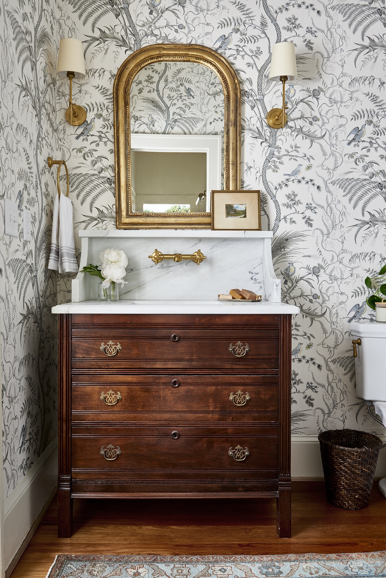 Historic guest bathroom remodel with antique natural wood dresser vanity, marble countertop, and floral wallpaper.