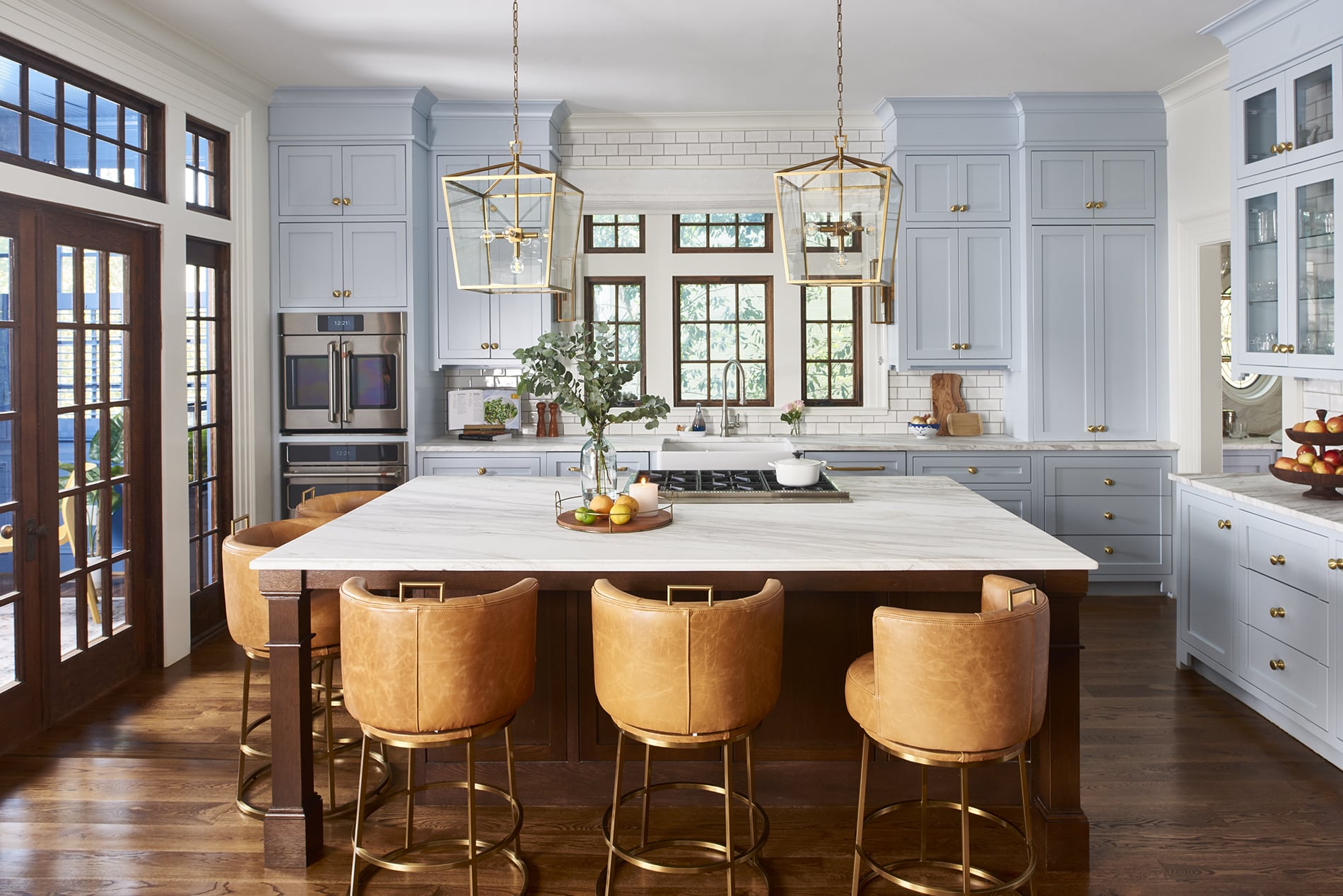 Transitional kitchen with light blue cabinets, large kitchen island with granite countertop, brass pendant lights and leather barstools.