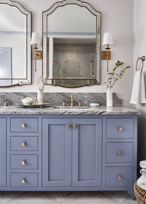 Transitional primary bathroom with dusty blue double vanity, marble countertop, and decorative mirrors.